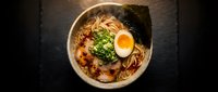 Steaming bowl of Japanese ramen with soft-boiled egg, chashu pork, nori, and green onions on dark slate background.