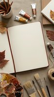 Open sketchbook surrounded by autumn art supplies, paint tubes, brushes and dried leaves on textured canvas background for creative projects and artistic inspiration.