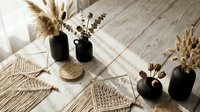 Boho home decor with dried pampas grass in black vases, macrame wall hangings and natural woven elements on wooden floor creating cozy interior design.