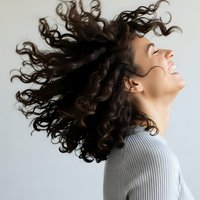 Young woman with curly brown hair in motion, head tilted back with joyful expression. Hair care, beauty and wellness concept for advertising campaigns.