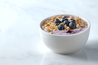 Creamy blueberry yogurt smoothie bowl topped with fresh berries, crunchy granola and oats on white marble background, healthy breakfast concept.