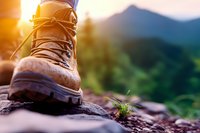 Brown leather hiking boot on mountain rock at sunset, with blurred nature background and warm sunlight creating atmospheric outdoor adventure scene.
