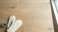 Pair of white knitted mittens with cable knit pattern placed on light wooden floor next to window, winter fashion and cozy home decor styling.