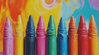 Vibrant melted wax crayons arranged in row against colorful blurred background showing rainbow spectrum of red, yellow, turquoise and pink colors in artistic composition.
