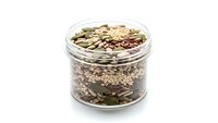 Glass jar filled with mixed seeds and nuts including pumpkin seeds, sunflower seeds, and various grains for healthy snacking and cooking recipes.