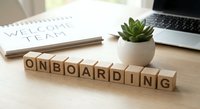 Wooden letter blocks spelling ONBOARDING on desk with laptop, notebook and succulent plant for business training and employee integration concepts.