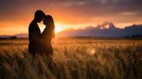 Romantic couple silhouette embracing in golden wheat field at sunset with mountains in background creating intimate moment for wedding concepts.