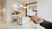Cropped hand holding blank white card in modern luxury bathroom interior with marble countertop and contemporary fixtures for business, hospitality, and retail messaging.
