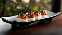 Spicy tuna sushi rolls topped with crispy tempura flakes and green onions served on modern black plate with steamed rice. Japanese cuisine on dark background.