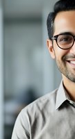 Portrait of a smiling male professional wearing eyeglasses and a light button-up shirt in a modern office setting, suitable for corporate, business, and professional website use.