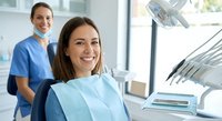 Happy female patient smiling in dental chair with dentist in background at modern clinic office for oral health checkup and treatment.