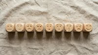Wooden cubes with carved emoji faces showing various emotions lined up on linen fabric, representing mood scale and mental health concepts.