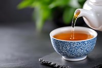 Pouring hot aromatic tea from white ceramic teapot into traditional blue and white porcelain cup with oriental pattern on dark stone background.