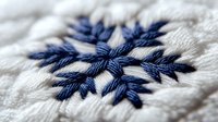 Handmade embroidery with navy blue thread forming a snowflake pattern on white fabric, showcasing traditional needlework and textile craftsmanship for winter-themed designs.