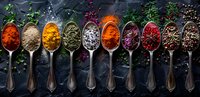 Vibrant colorful spices and herbs in vintage silver spoons arranged in row on dark background, overhead view. Culinary seasoning collection for food styling.