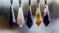 Collection of polished gemstone crystal pendants on black cords featuring various natural stones in teardrop shapes for jewelry making and spiritual healing.