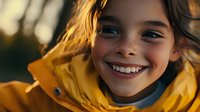 Cheerful young Hispanic girl with freckles wearing yellow raincoat smiles brightly at sunset, showing authentic joy and innocence in natural outdoor lighting.