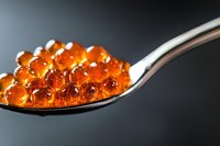 Orange caviar pearls on silver spoon against dark background. Molecular gastronomy spheres for gourmet cooking and fine dining presentation.