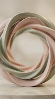 Abstract ceramic sculpture with flowing curved ribbons in soft sage green and blush pink tones, isolated on neutral background, suitable for modern interior design and contemporary art projects.