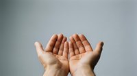 Open cupped hands gesture showing palms up in receiving position against neutral gray background for prayer, giving, or support concepts.