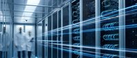 Young male technician in white coat inspecting server racks with glowing blue network cables in modern data center facility for IT infrastructure and cloud computing.