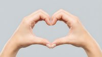 Two hands forming a heart shape gesture on a gray background, symbolizing love, care, and connection.