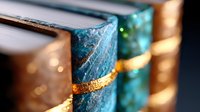 Turquoise and gold marbled books with decorative spines arranged on shelf, creating elegant bokeh effect in soft lighting. Vintage aesthetic for luxury interior design.