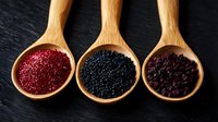 Colorful quinoa grains and black lentils displayed in wooden spoons on dark slate surface for healthy cooking and nutrition concepts.