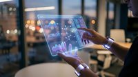 Businessman using futuristic transparent tablet with holographic financial data charts and graphs in modern office environment at evening.