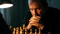 Senior Caucasian man concentrating deeply while playing chess under warm lamp light, hands clasped in thoughtful pose during strategic board game session.