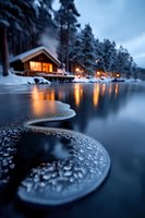 Cozy wooden cabin glowing warmly by frozen lake at dusk, with illuminated windows reflecting on dark water surface through curving ice formations and snow-covered pines.