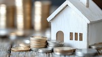 White wooden house model surrounded by stacked gold and silver coins on rustic wooden surface, representing real estate investment and property finance.