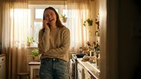 Young woman talking on phone in cozy kitchen with warm lighting and plants, casual lifestyle moment for communication and home living concepts.