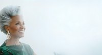 Senior woman with gray hair and pearl earrings wearing green top, smiling in profile against white background. Suitable for healthcare, wellness, aging, lifestyle and portrait projects.