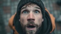Surprised bearded man in winter knit hat with wide eyes and open mouth showing shock or amazement against blurred urban background for advertising campaigns.