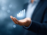 Businessman in dark suit holding glowing digital bar graph chart showing growth trend, floating above palm against blurred blue background with bokeh effect.