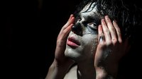 Dramatic portrait of woman with dark artistic makeup and wet hair holding hands near face against black background, expressing deep emotion and vulnerability.