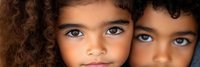 Two young mixed-race children with curly hair and striking blue eyes looking directly at camera in close-up portrait showing innocence and wonder.