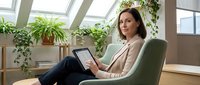 Professional businesswoman using tablet in modern office with plants and natural light for remote work and digital communication.