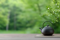 Black ceramic teapot on bamboo mat against blurred green garden background creates zen atmosphere for meditation and tea ceremony concept.
