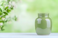 Empty glass mason jar on white surface against soft green spring background with blurred white flowering branches, suitable for food and beverage packaging.