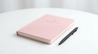 Closed pink notebook with pen on white surface, isolated for design mockups, stationery branding, and business presentations.