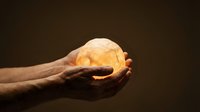 Hand holding glowing golden orb against dark background, symbolizing energy, innovation, and success for business and technology concepts.