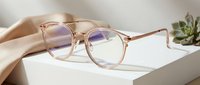 Clear rose gold-toned eyeglasses with blue light filtering lenses held by hand against white background, suitable for eyewear advertising and optical design projects.
