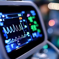 Medical monitor displaying vital signs with ECG waveform and digital parameters in intensive care unit, showing patient health data with colorful bokeh background.
