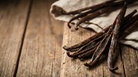 Aromatic vanilla beans and pods scattered on rustic wooden surface for baking and culinary applications in natural kitchen setting.