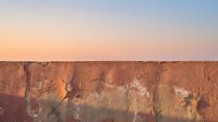 Dramatic sunset light illuminates weathered terracotta cliff face with layered geological formations and natural erosion patterns, suitable for travel, nature, and environmental design projects.