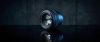 Professional camera lens with blue and black metallic finish isolated on dark reflective surface, suitable for photography equipment marketing and tech product design.