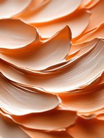 Smooth flowing waves of peach and coral cream create abstract organic shapes with soft shadows and highlights, showcasing luxurious cosmetic texture.