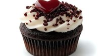 Chocolate cupcake topped with vanilla frosting, chocolate sprinkles and red heart decoration on white background, close-up view for Valentine's Day or romantic dessert menu.